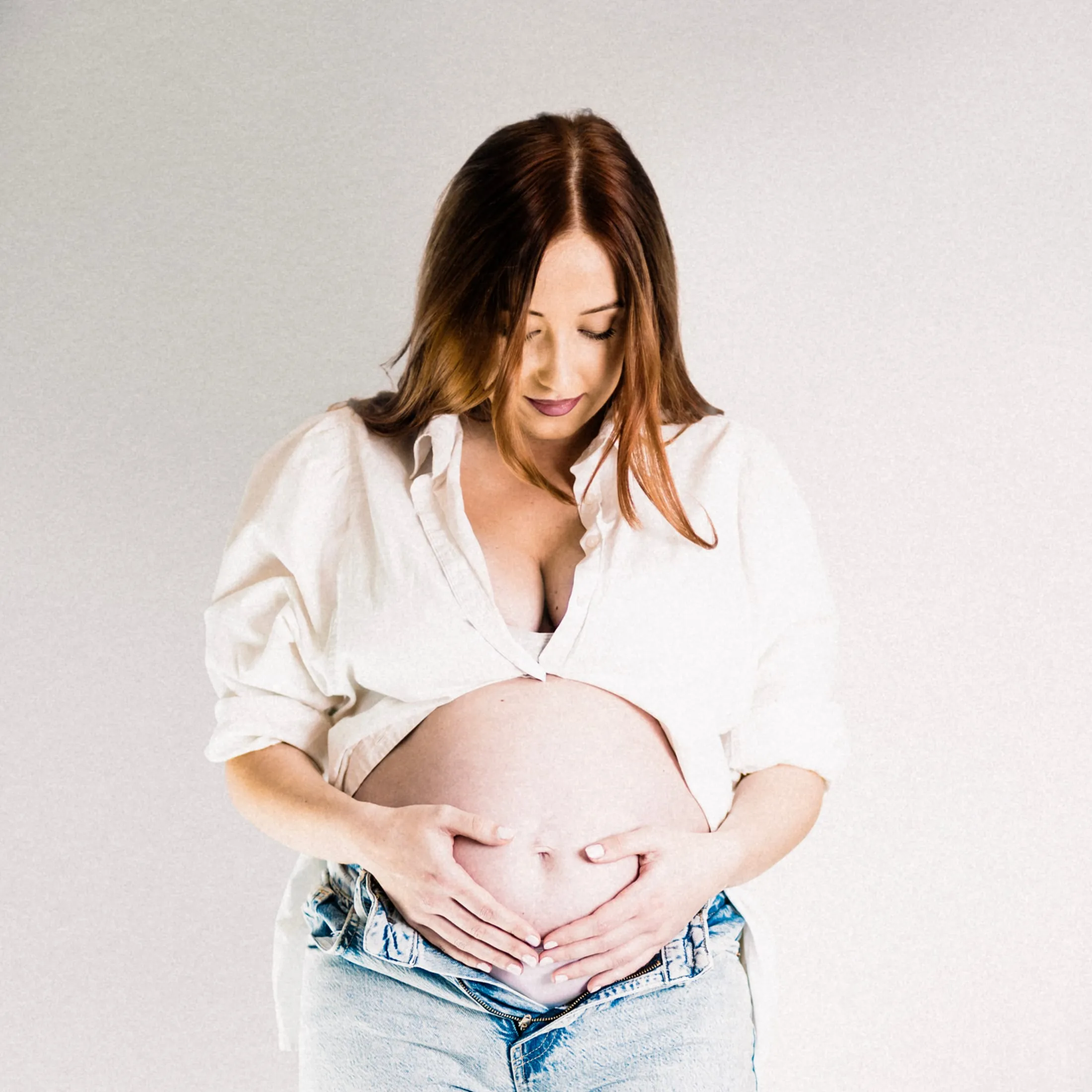 Expectant mother cradling her bump with both hands, looking down, in soft studio light