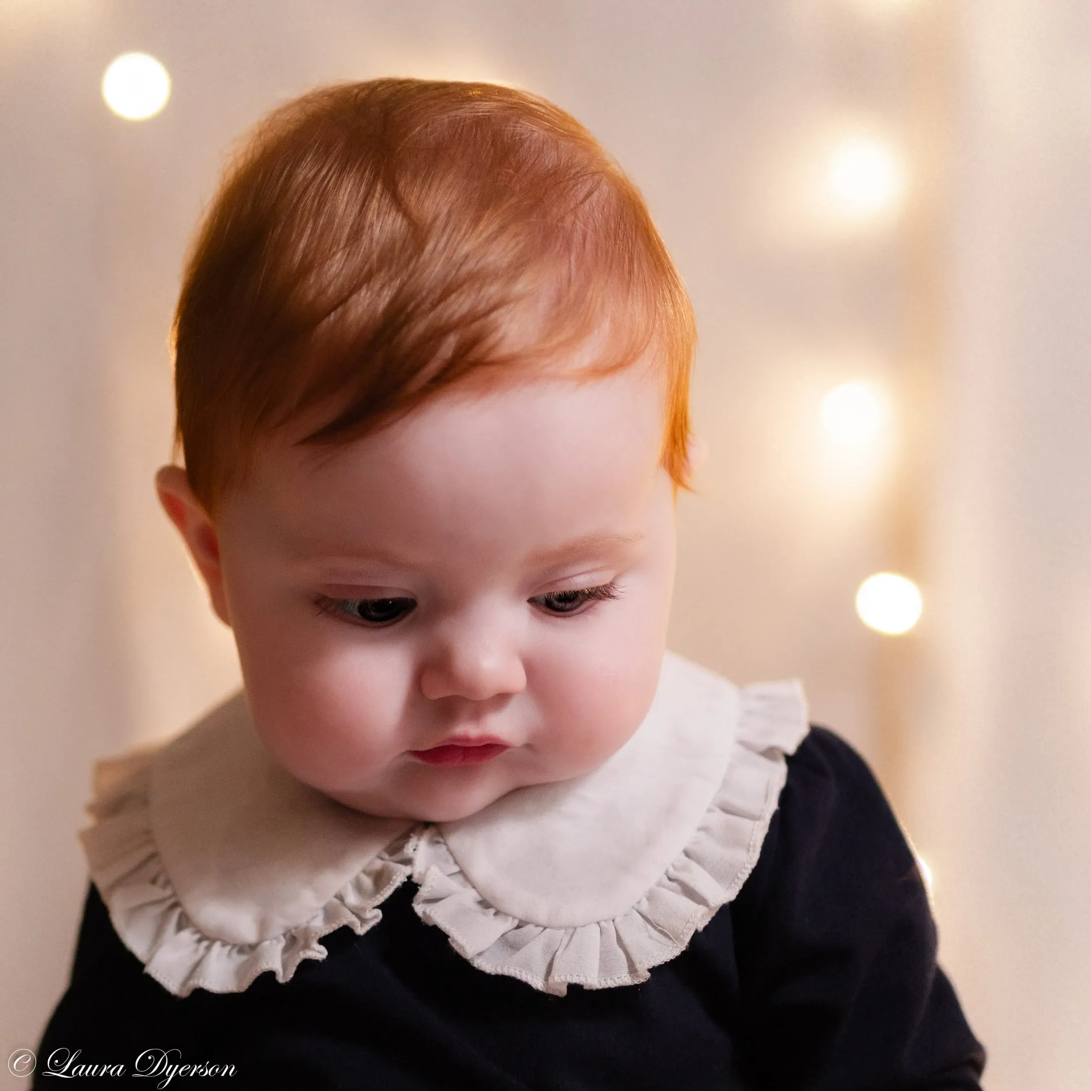 Red-haired baby looking down, festive bokeh